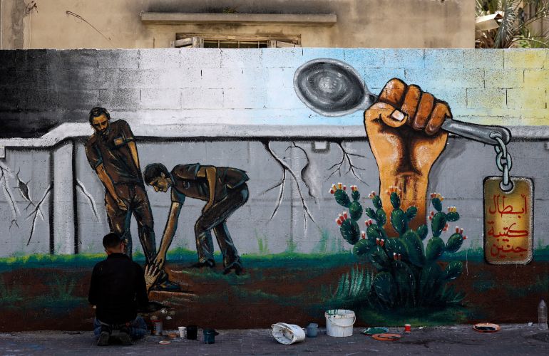 An artist works on a mural painting glorifying six Palestinian prisoners who escaped from Israel's Gilboa prison in September 2021 with the help of the humble spoon [Mahmud Hams/AFP]