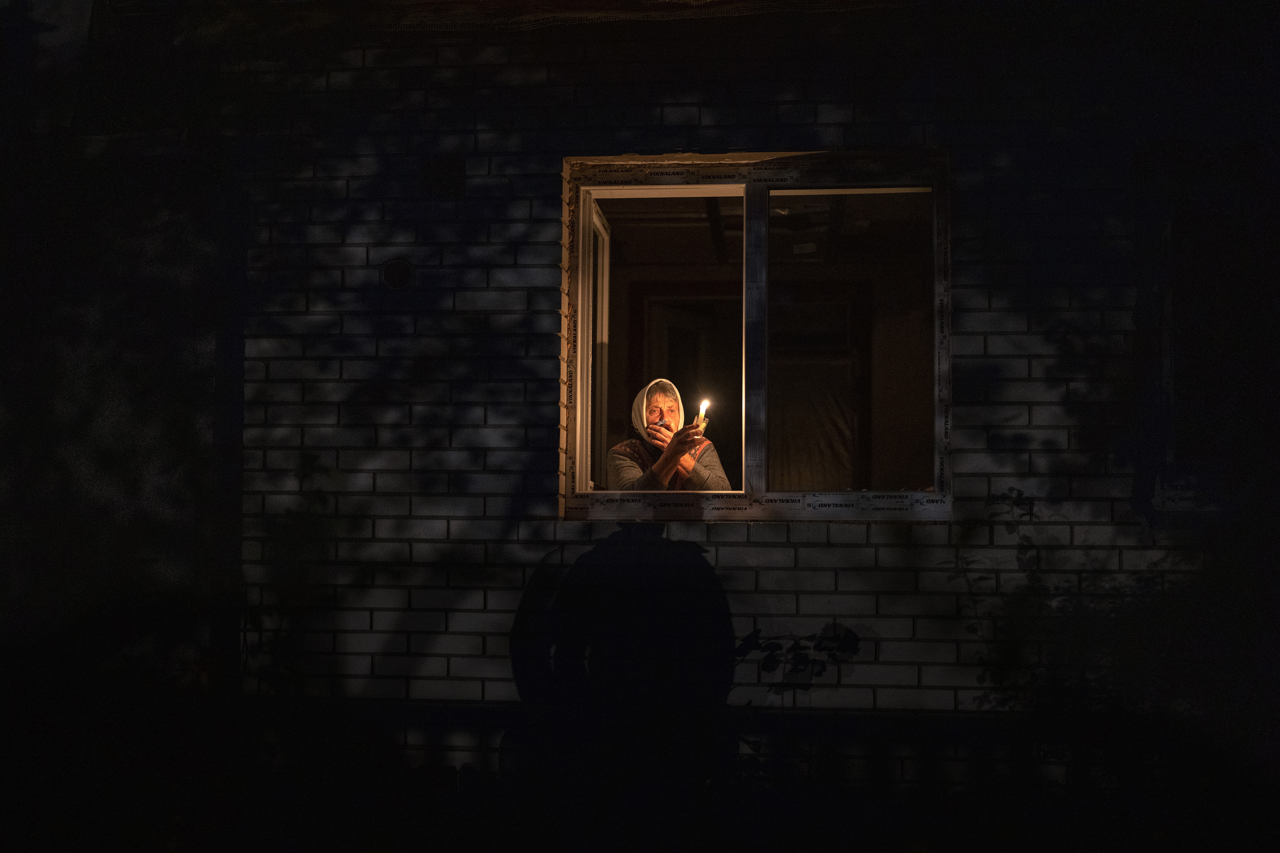 Catherine, 70, looks out the window while holding a candle for light inside her house during a power outage.