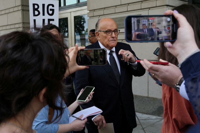Onlookers and reporters point cellphones and microphones at Rudy Giuliani as he leaves a US district court.