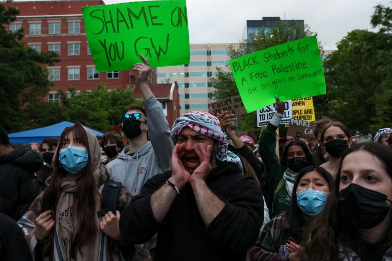 Students and others at a demonstration at George Washington University. One is carrying a banner reading 'Shame on you GW'. Another is carrying a placard reading 'Black students a free Palestine. Our struggles are connected' A man is shouting with his hands cupped around his mouth. Most are wearing face masks.