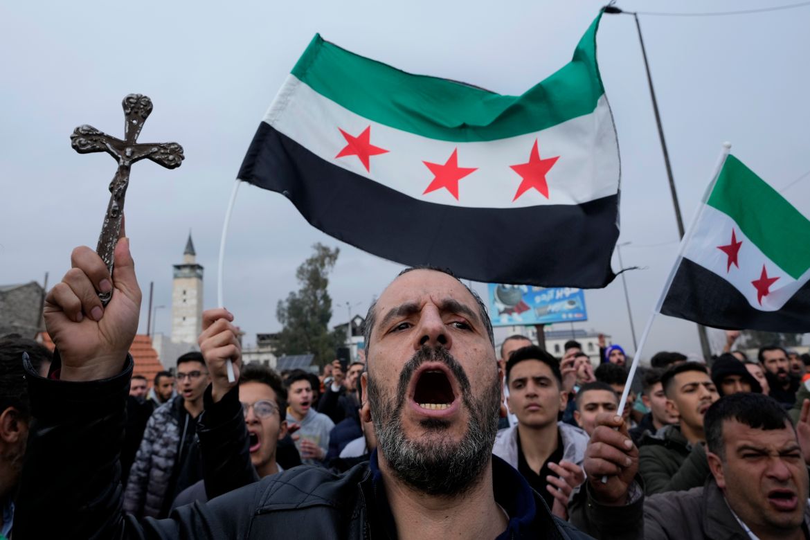 A Syrian Christian man holds up a cross and shouts slogans in Damascus